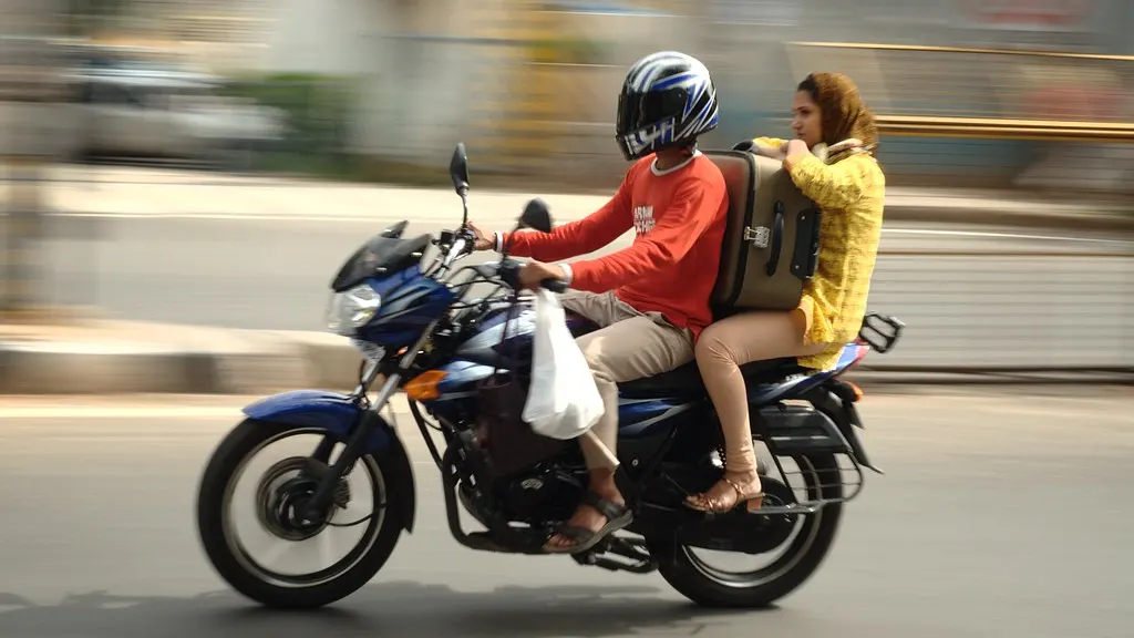A motorbike rider in a helmet carrying a pillion passenger through city traffic