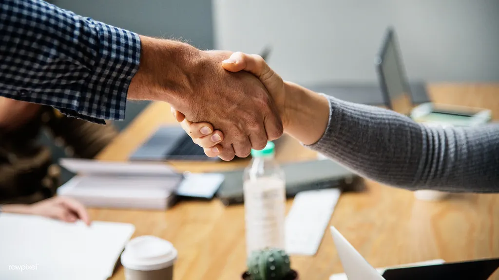 Two people shaking hands across a meeting table