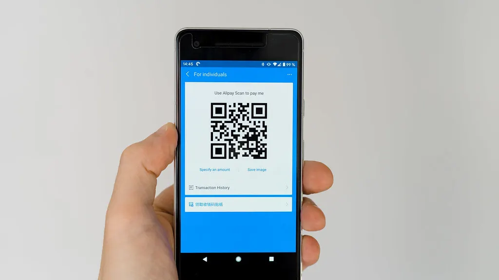 A hand holding a phone showing a QR code for payment
